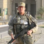 ff87d7b72a6f4666962b612fbaea243d FTC Safeguards Rule Checklist for Small Businesses (Plain-English) 3 Compliance A soldier from our team stands outdoors in uniform, holding military equipment, with a building and palm trees framing the background.
